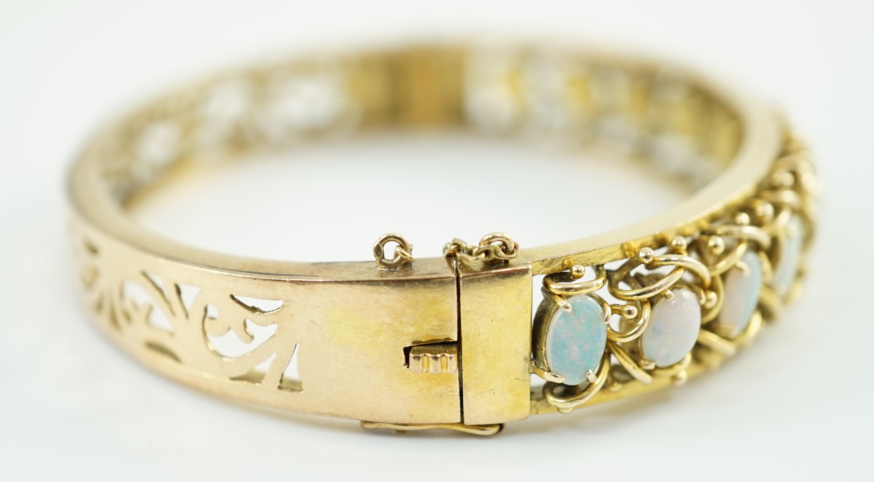 A pierced gold and twelve stone oval white opal set hinged bangle